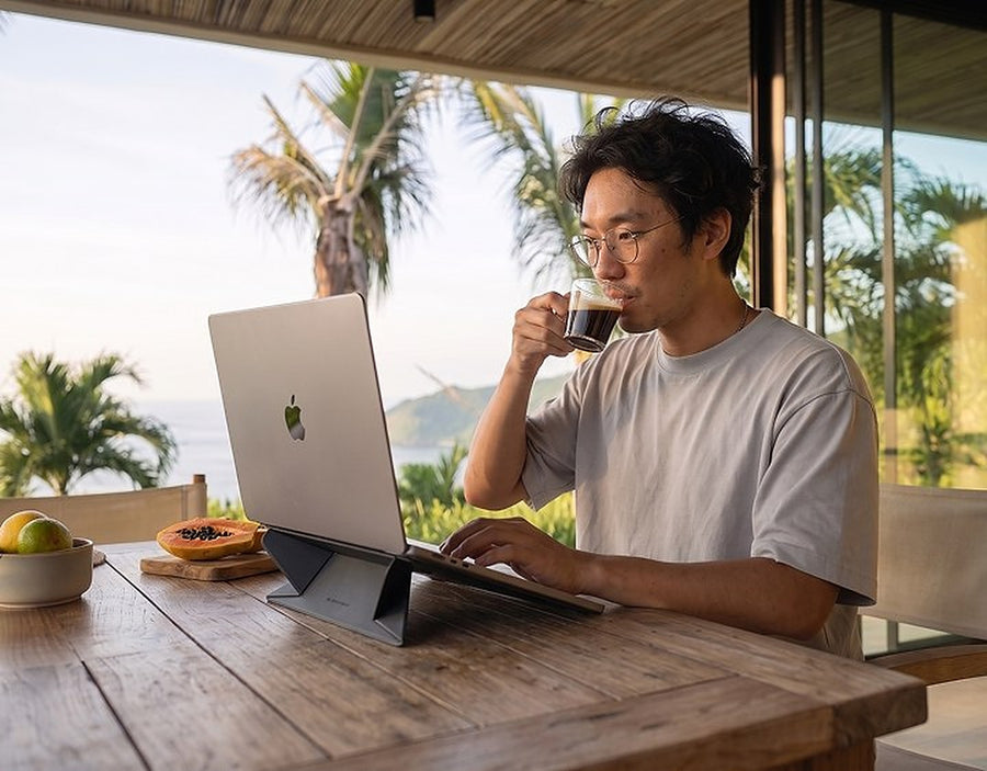 Man drinkt koffie en werkt op een laptop met standaard op een tropisch terras