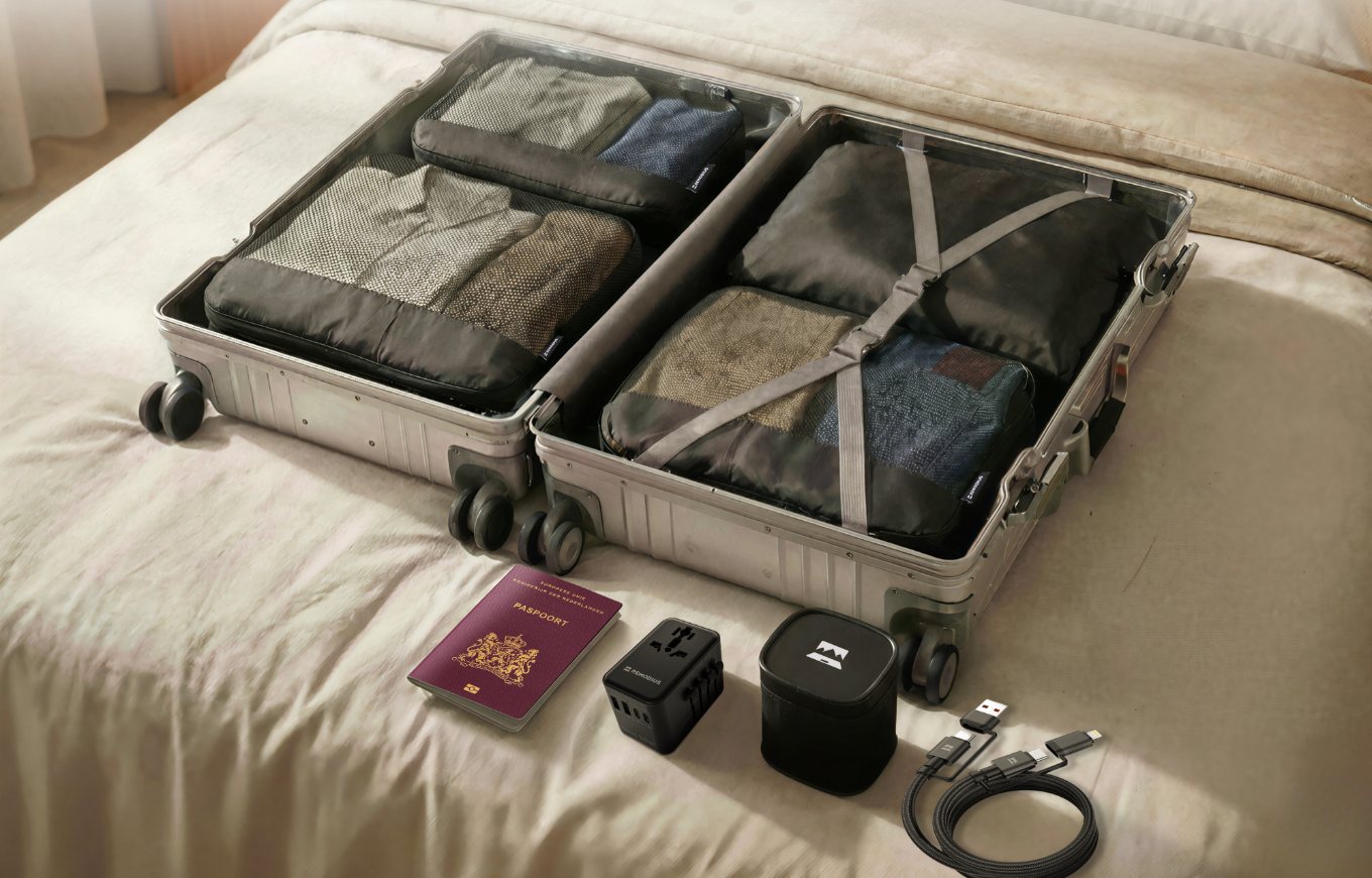 Open handbagagekoffer op een bed met Remodius packing cubes, paspoort, wereldstekker en kabel